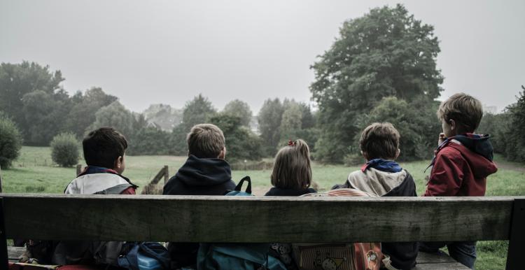 five children sat on a bench with backs to camera 