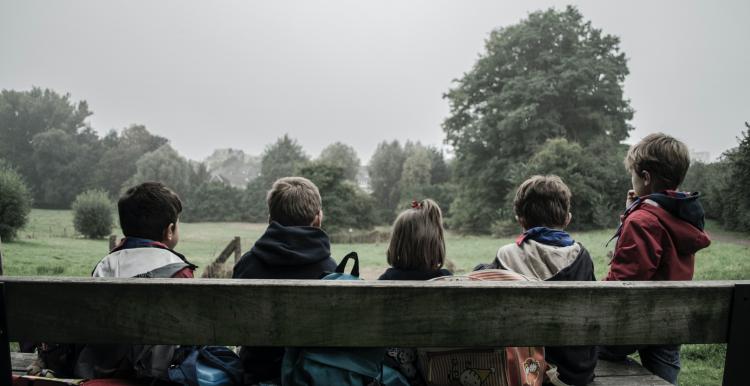 five children sat on a bench with backs to camera