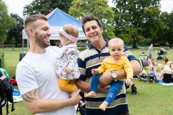 two men on a park holding babies 