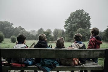 five children sat on a bench with backs to camera 