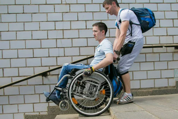 A young man helping another in a wheelchair 
