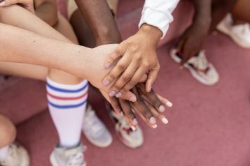 Faceless multiracial sport team stacking hands on court. Four hands are in a pile and there is a blurred background with legs and trainers.